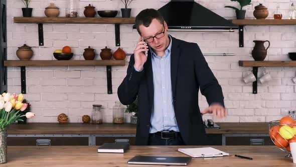 Serious Angry Businessman in Glasses and Suit is Angrily Talking on the Phone at Home in the Kitchen alt