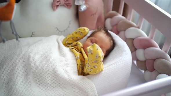 Newborn in a Yellow Jumpsuit Lies in a Retainer of the Child in a Crib alt