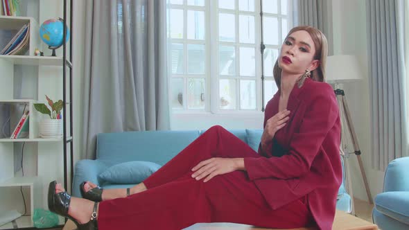 Young Fashion Transgender Woman Wearing Red Clothes Sitting On Table And Posing In Home alt