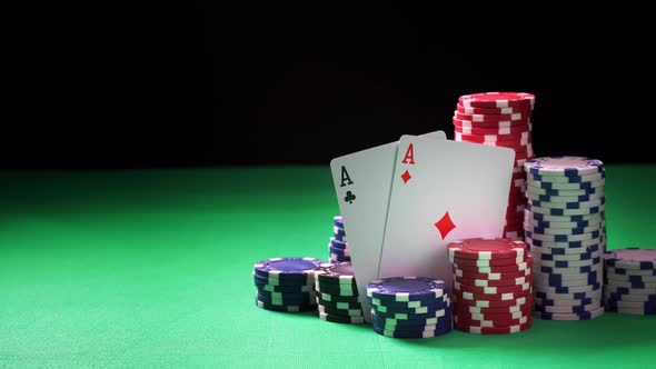 Stacks of Poker Chips and Two Aces on Green Table and Black Background in Close-up alt