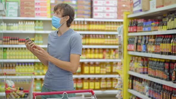 An Alarmed Man Wears a Medical Mask Against Coronavirus While Purchasing Food in a Supermarket or alt