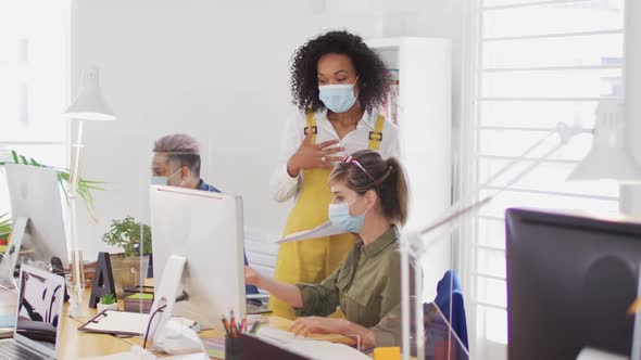 Office colleagues wearing face masks discussing over computer at office alt