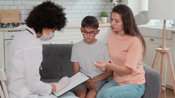 Afro American Woman Doctor in Mask Looks at the Thermometer Reading of a Child and Writes a alt