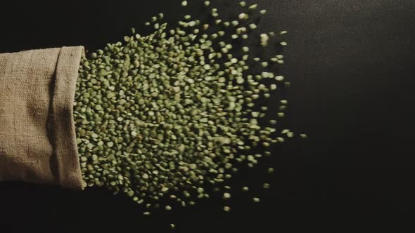Green Peas Pour Out Of Falling Sack On Black Table