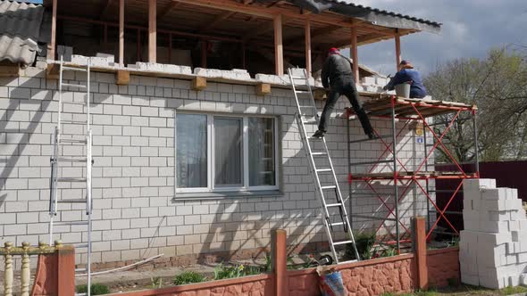 Two workers are laying white bricks at height at construction of house