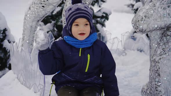 A Boy Sits Near a Beautiful Statue and Throws Snow Into the Camera