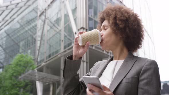 Afro American businesswoman in city using smart phone with takeaway coffee