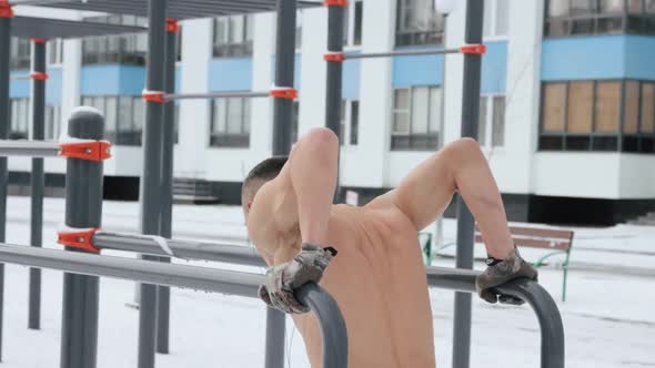 Muscular man training topless on sports field in winter