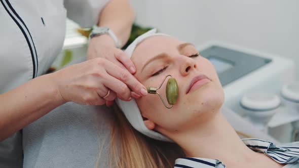 Close-up Shot of Facial Massage with a Jade Roller on Woman's Face at Beauty Salon alt