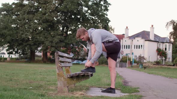 Young Attractive Man Tying His Shoes on a Bench Before He Sets of For a Run alt