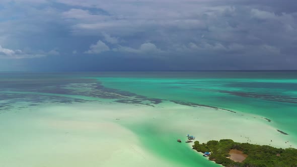 Aerial shot revealing a small island in the Caribbean. Sea with different colors and black clouds in alt