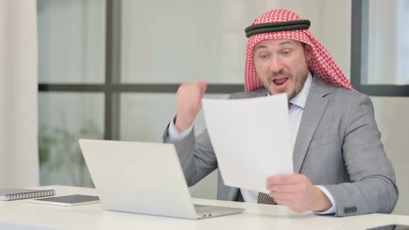 Middle Aged Arab Businessman with Laptop Celebrating Success while Reading Documents alt