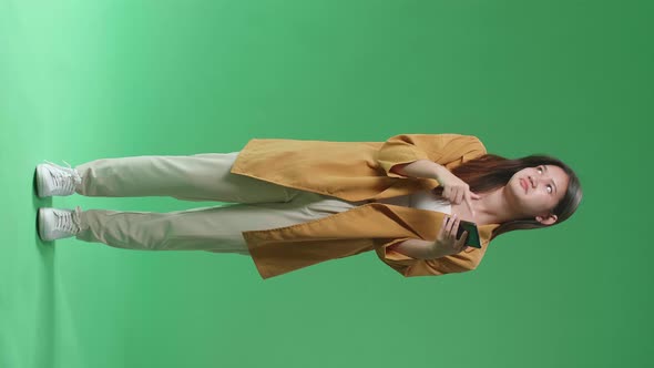 Full Body Of Young Asian Woman Emotionally With Phone While Standing In The Green Screen Studio alt