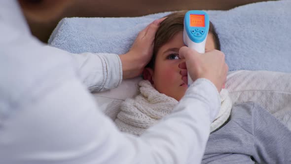 Boy Feeling Unwell Has High Temperature Measured with Noncontact Thermometer in Degrees Celsius alt