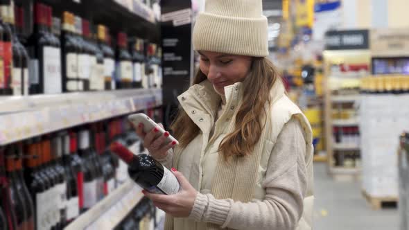 A Young Woman Scans the Code on a Bottle of Wine Using Her Smartphone alt