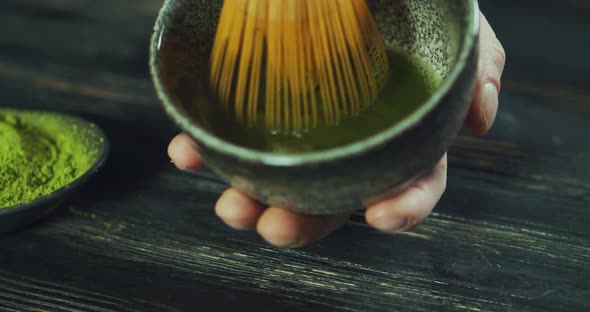 Man Preparing Green Tea Matcha in a Bowl on Black Wooden Table. Man Add Matcha Green Tea Powder Into