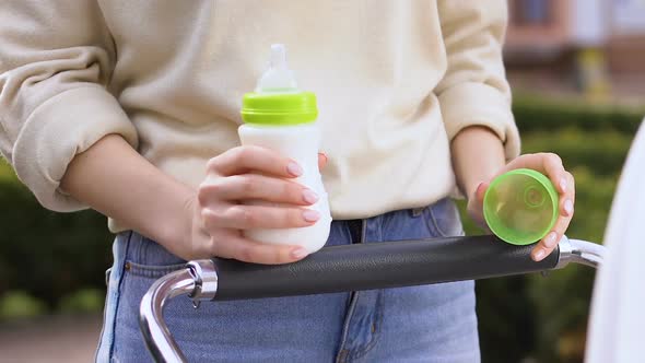 Mother Feeding Baby in Carriage With Infant Formula, Vitamin Milk for Newborns alt