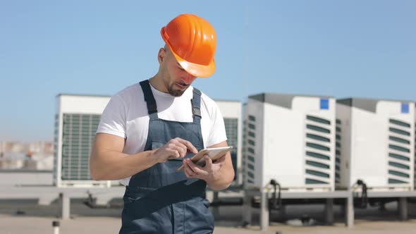 Portrait of a Serious Young Engineer is Working on the Tablet and Looking at the Camera alt