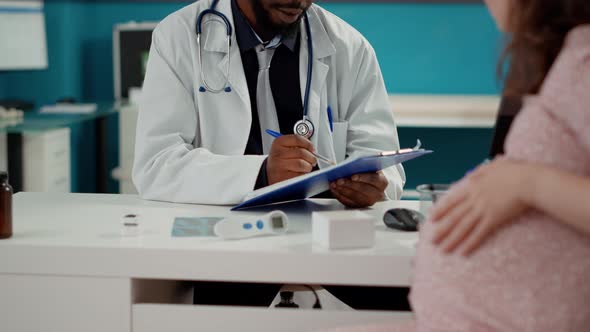 African American Medic Taking Notes at Consultation with Pregnant Person alt