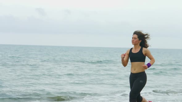 Serious Young Woman With Concentrated Face Expression Running Along Sea Beach alt