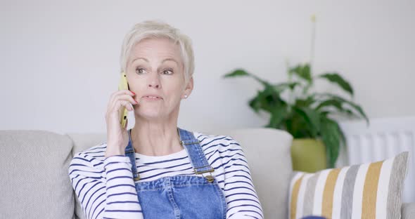 Mature woman sitting on sofa talking on the phone alt