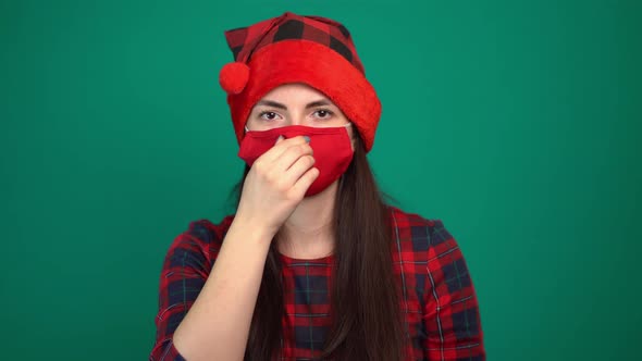 Portrait of Young Woman in Santa Hat Wears a Red Medical Mask, Looking at Camera alt