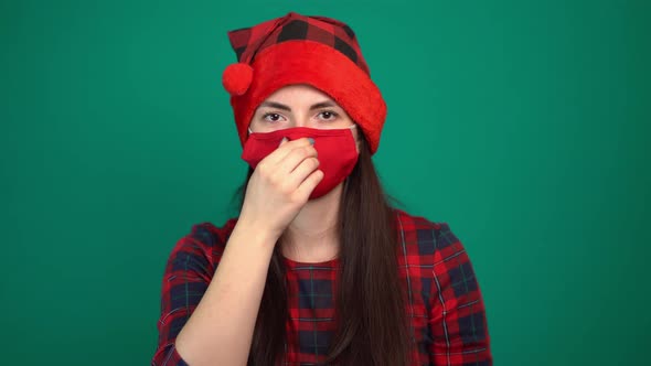 Portrait of Young Woman in Santa Hat Wears a Red Medical Mask, Looking at Camera
