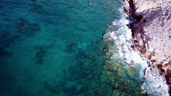 Aerial Footage of Surge of Waves at a Rocky Coast with Clear Blue Water