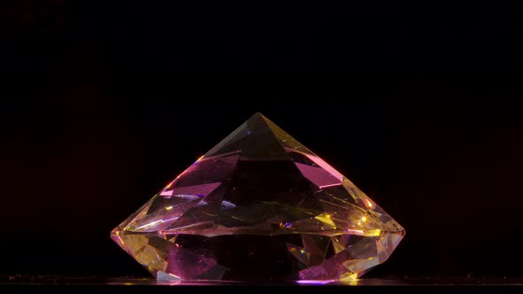 One Large Diamond Stone with Many Facets Glitters in the Rays of Light and Rotates Against a Black alt
