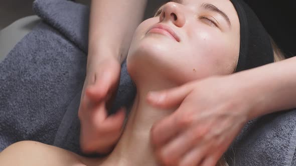 Attractive Woman in a Beauty Salon Lies on the Bed and Receives a Massage on the Neck and Decollete alt