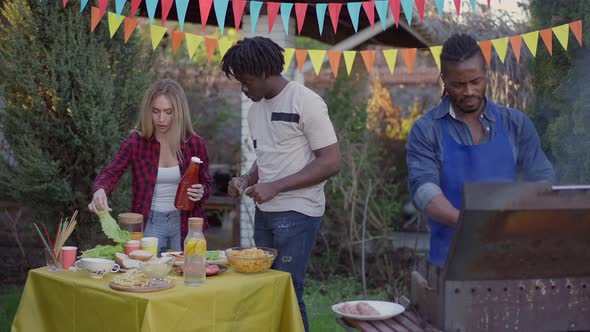 Three Positive Multiracial Friends Preparing Picnic Table in Slow Motion Outdoors alt
