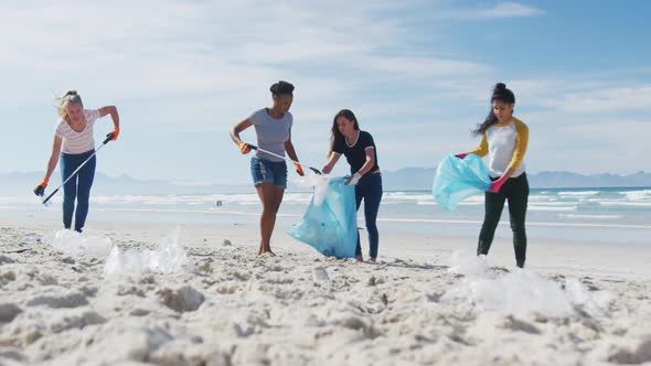 Diverse group of female friends putting rubbish in refuse sacks at the beach alt