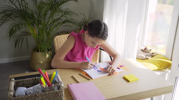 Teenager Girl Draws in Notebook Sitting at Wooden Table