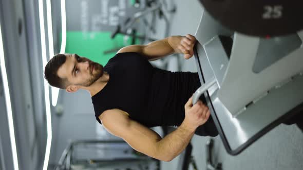 Verical Shot of Man Puts Additional Weights on a Barbell and Doing Leg Exercises alt