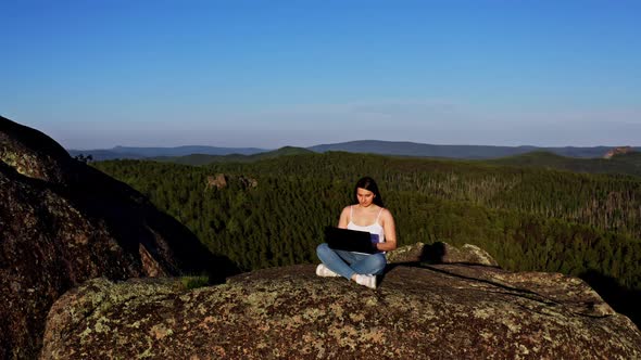 A Young Beautiful Woman with a Laptop on a Rock