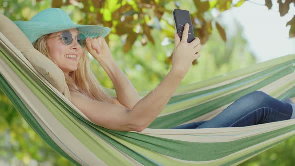 Smiling blonde woman with sunglasses using smartphone