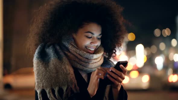 Woman holding smartphone at the evening street. 