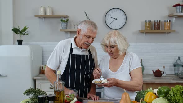 Senior Couple in Kitchen. Grandmother Feeding Grandfather with Raw Sprouts Buckwheat with Nuts alt