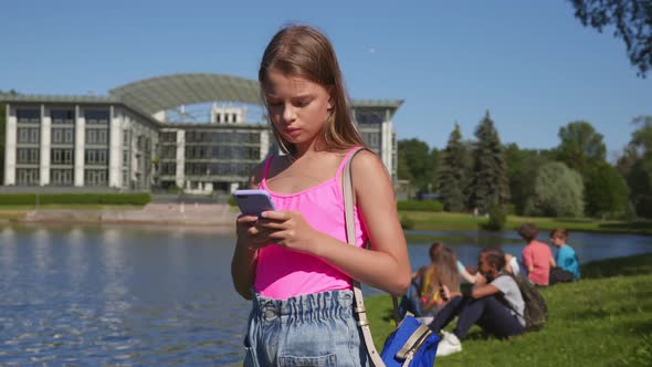 Caucasian Preteen Girl Using Mobile Phone Standing in Summer Park
