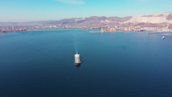 White Cargo Vessel Sails Crossing Blue Ocean Against Coast alt