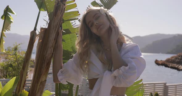 Blonde girl enjoying summer and hiding from the sun in palm leaves. Vacation holidays alt
