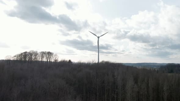 Wind turbine spinning fast behind a dark, dry forest in western Germany. Aerial ascending tracking s alt