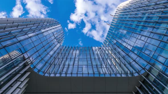 Time lapse, looking up at a glass-covered skyscraper, reflecting the blue sky and passing clouds alt