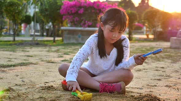Asian Girl Playing Sand In Playground Under Sunset alt