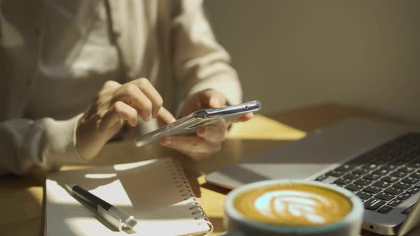Young woman with cup of coffee using mobile phone and working on laptop at coffee shop