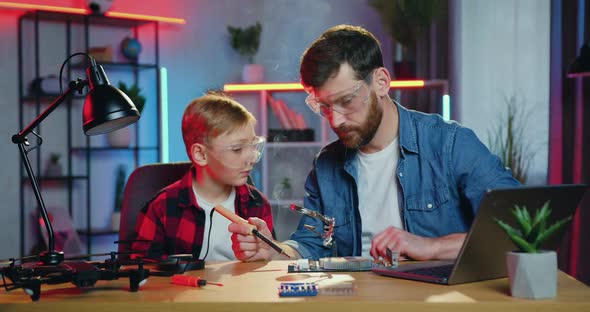 Teen Boy in Protective Glasses Looking through Magnifying Glass alt