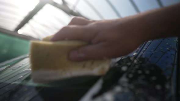 Male Caucasian Hand Rubbing Car Wash Shampoo on Windshield with Sponge in Slow Motion alt