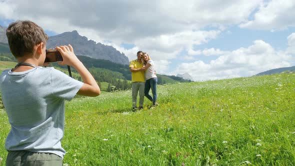 Boy (8 to 9) photographing parents in Alpine meadow, Alta Badia, Italy