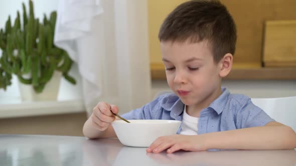 Small Hungry Boy Eating Tasting Sweet Corn Flakes with Milk at Morning alt