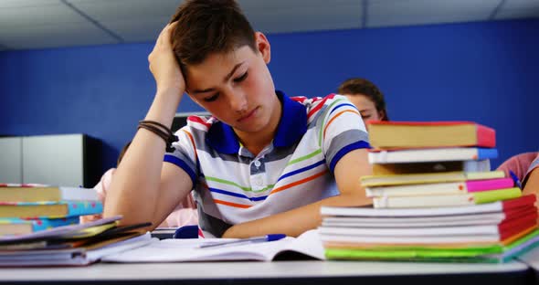 Thoughtful schoolboy sitting in classroom alt
